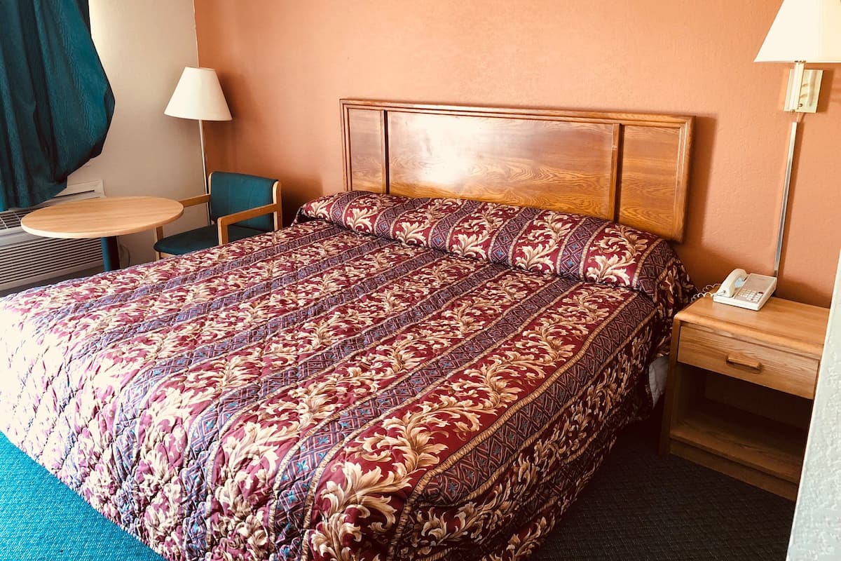 A hotel room with a large bed, a bedside table with a lamp, a chair, and a small table.