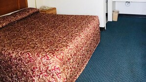 A hotel room with a large bed, a bedside lamp, a framed picture on the wall, a bathroom with a sink and mirror, and a carpeted floor. - Rest Inn Motel (Palestine)