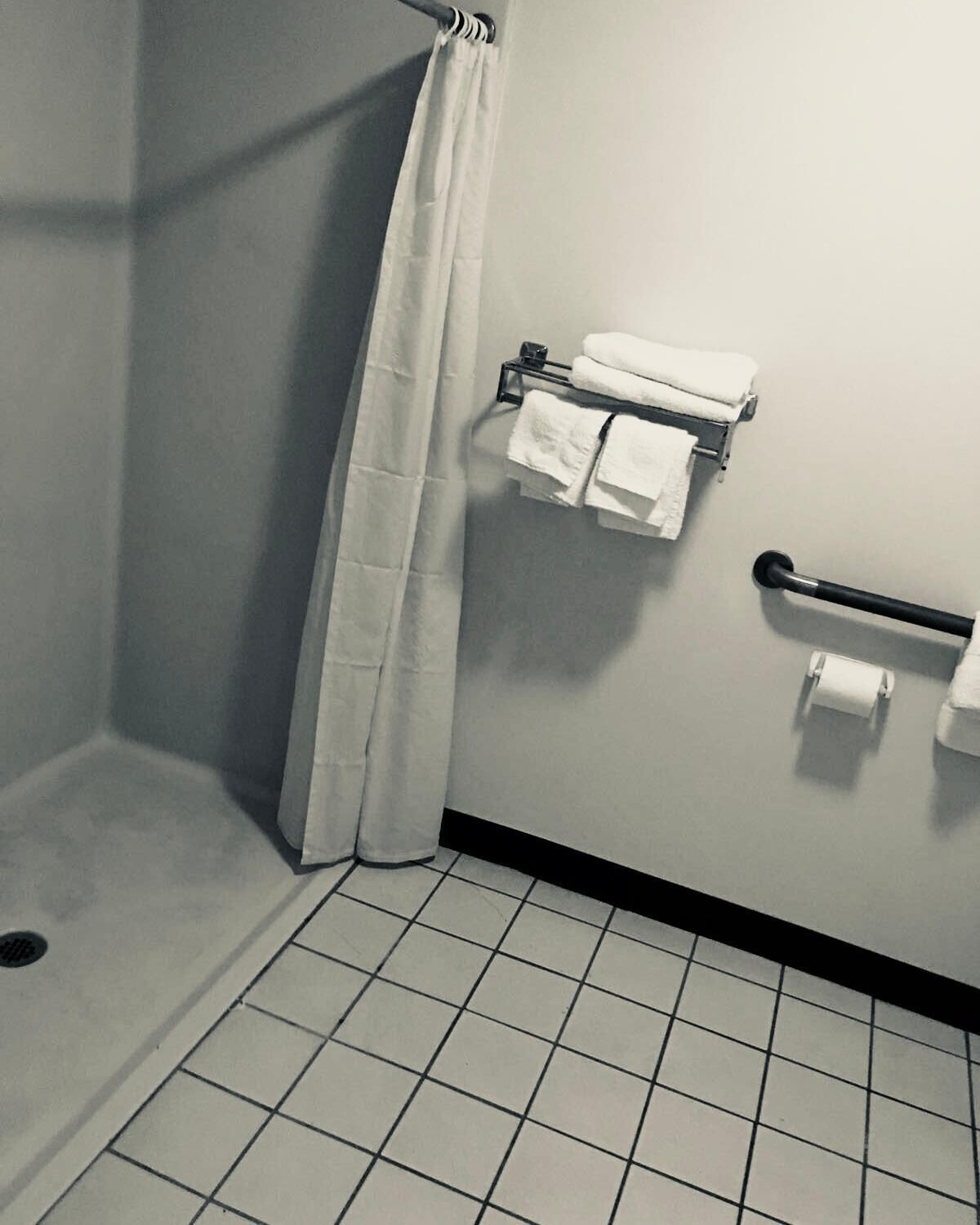 A bathroom with a shower, a towel rack, and a toilet paper holder.