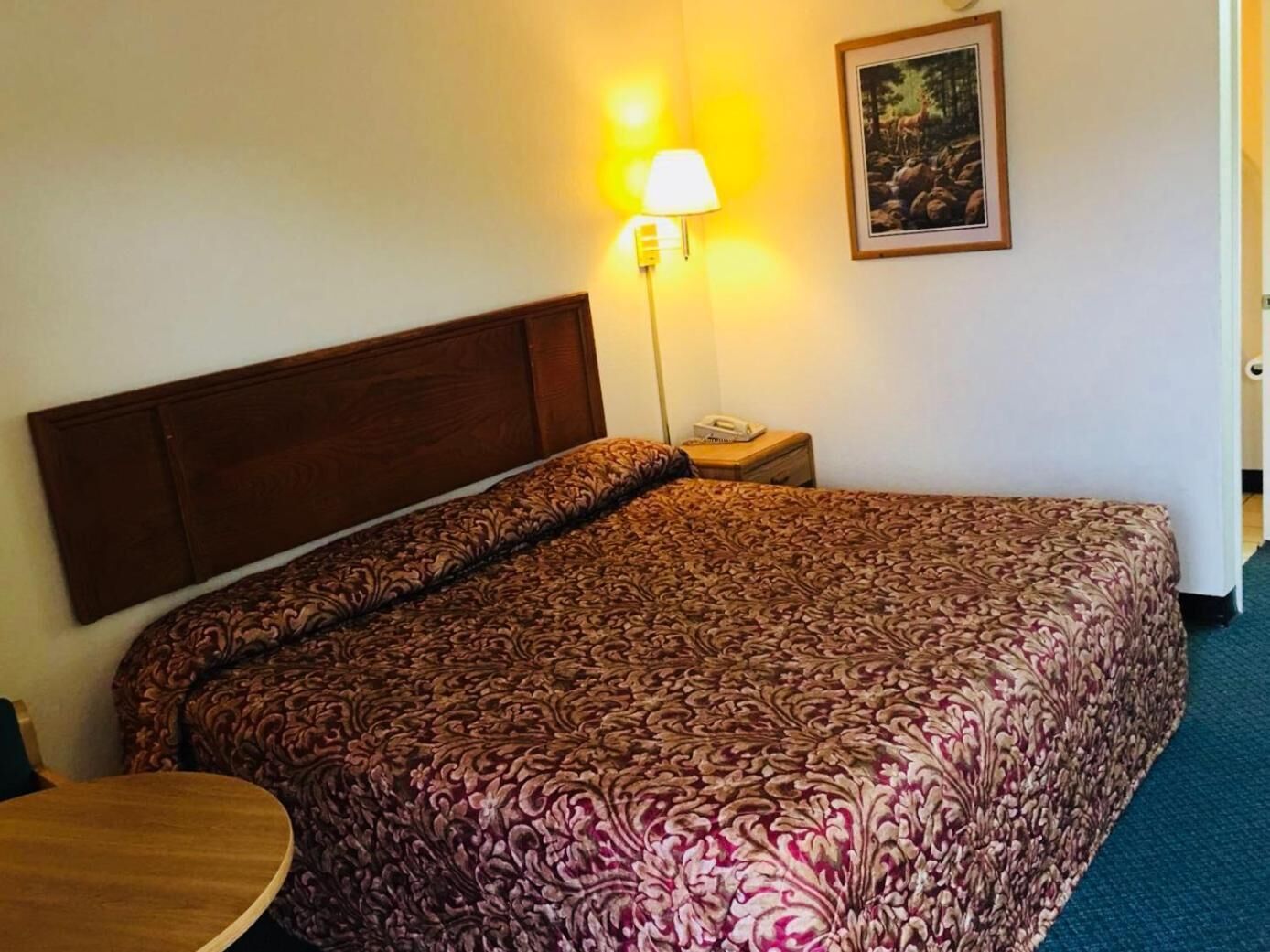 Hotellihuone, jossa on suuri sänky, yöpöytä, lamppu ja seinällä oleva kehystetty kuva.