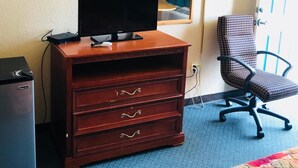 A hotel room with a wooden dresser, a television on top, a chair, a desk, and a lamp. - Rest Inn Motel (Palestine)
