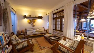Una sala de estar acogedora con muebles de madera, una estantería y un gran ventanal con cortinas.