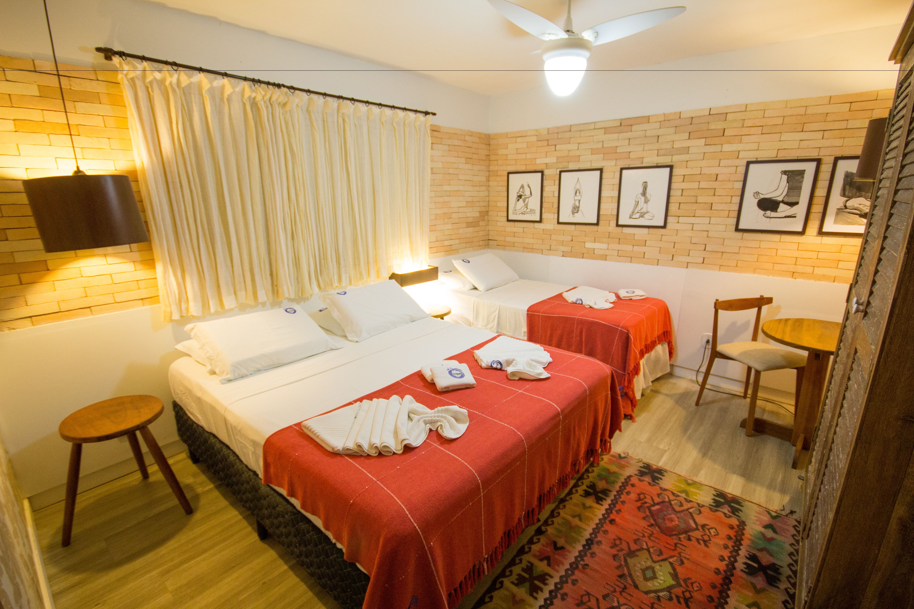Habitación de hotel con dos camas, piso de madera, pared de ladrillo y ventilador de techo.