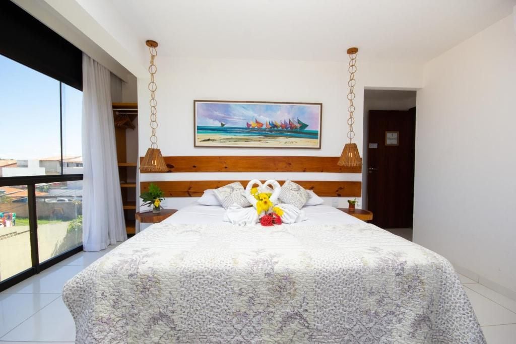 Quarto de hotel com uma cama grande, um quadro sobre a cama e vista pela janela.