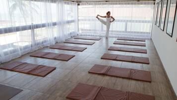 Un estudio de yoga con varias colchonetas dispuestas en el suelo, amplias ventanas con cortinas translúcidas y cuadros en la pared.