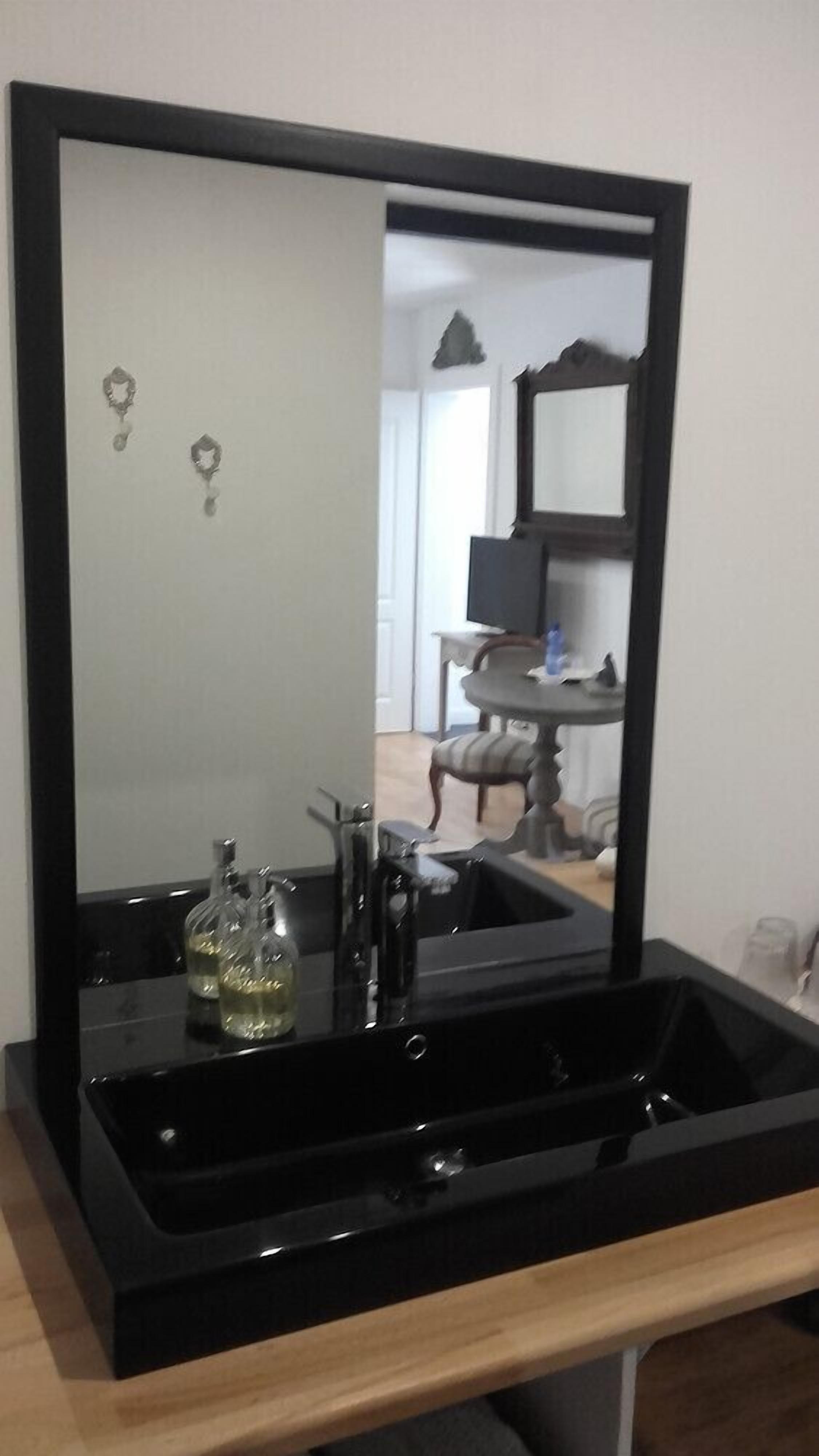 Un bagno con un lavandino nero, uno specchio e una bottiglia di sapone per le mani.