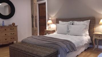 A bedroom with a bed, two bedside tables, a dresser, a mirror, and a wicker bench.