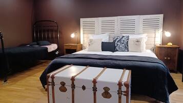 Un dormitorio con una cama grande, una cama más pequeña, una mesita de noche, una lámpara y una maleta.