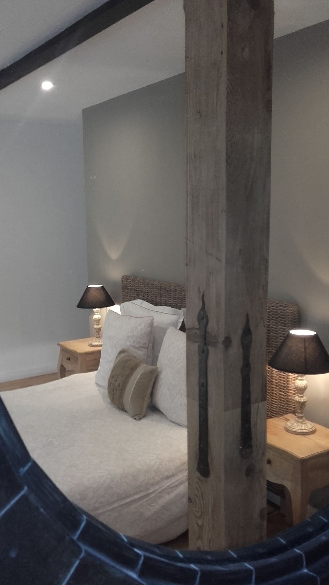 Un dormitorio con una cama grande, dos mesitas de noche con lámparas, un pilar de madera y un techo curvo.
