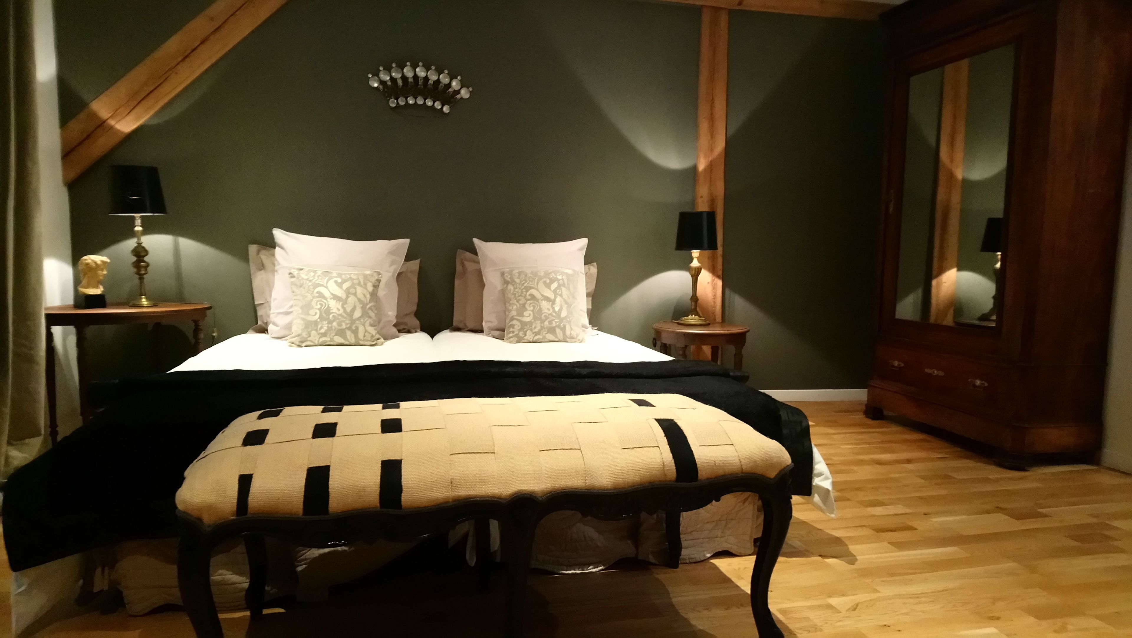 Un dormitorio con cama, dos mesitas de noche con lámparas, un banco, un espejo y suelo de madera.