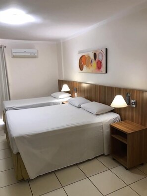 Une chambre d’hôtel avec deux lits, une tête de lit en bois, un climatiseur fixé au mur, une lampe de chevet et un tableau.