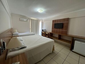 Une chambre d’hôtel avec deux lits, un téléviseur fixé au mur, un bureau avec une chaise et un réfrigérateur.