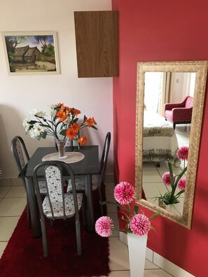 Un coin repas comprenant une table, des chaises, un vase avec des fleurs, un miroir et un tableau encadré accroché au mur.