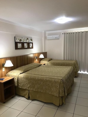 Une chambre d’hôtel avec deux lits, une tête de lit en bois, un climatiseur fixé au mur et une fenêtre avec des rideaux.