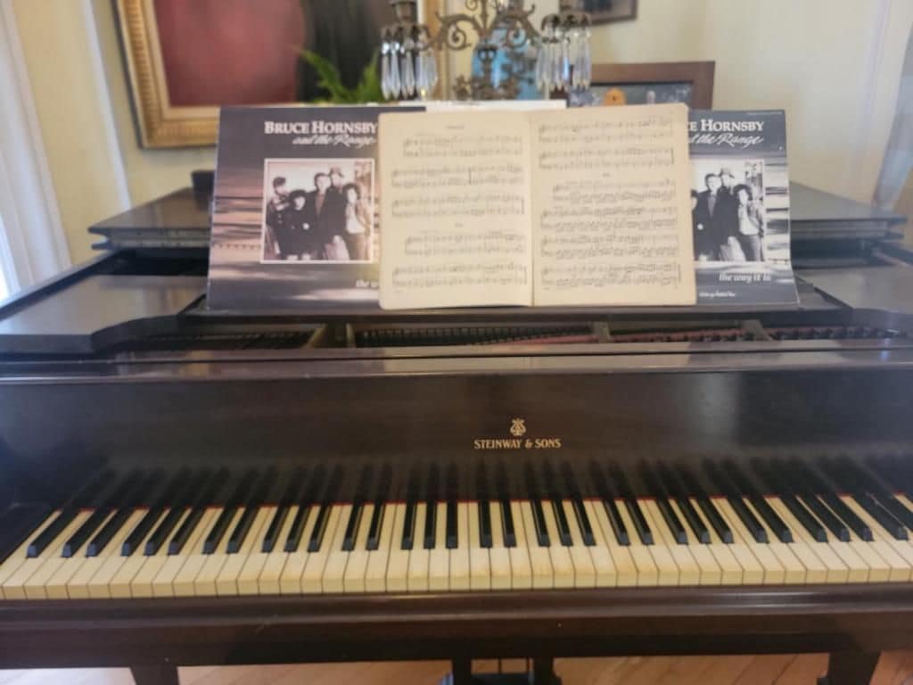 A grand piano with sheet music titled 'Bruce Hornsby' in front of a framed picture.