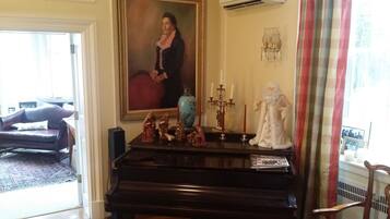 Un salón con un piano, un retrato grande y una estatua de un personaje religioso.