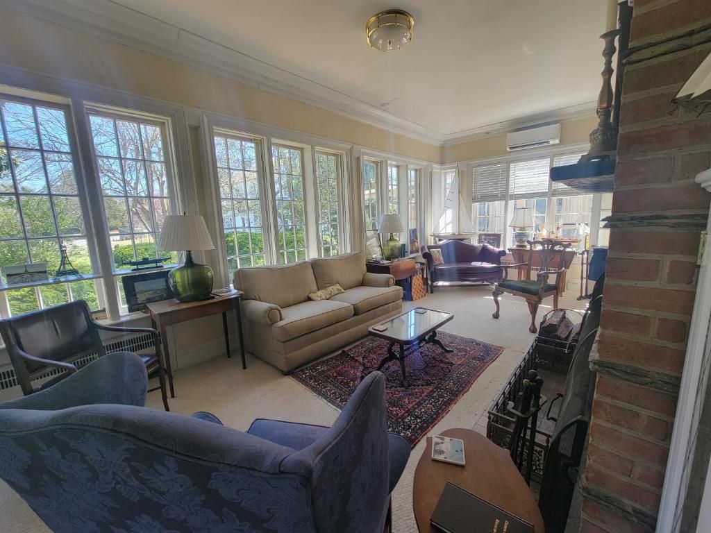 Een ruime woonkamer met een bank, fauteuils en een salontafel. Grote ramen zorgen voor natuurlijk licht en uitzicht op het groen.