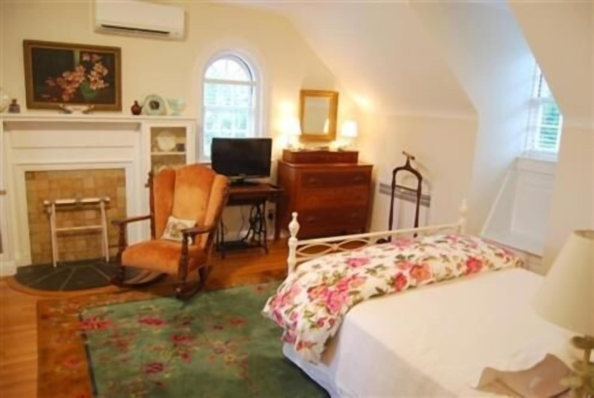 Un dormitorio con cama, una silla, un escritorio, un aparador y una chimenea.