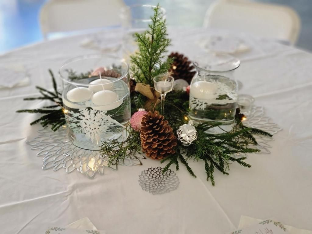A table set with clear glass candle holders, pine cones, and greenery, suggesting a festive or holiday theme.