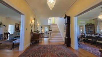 A spacious hallway with a grand staircase, wooden flooring, and a large ornate rug.
