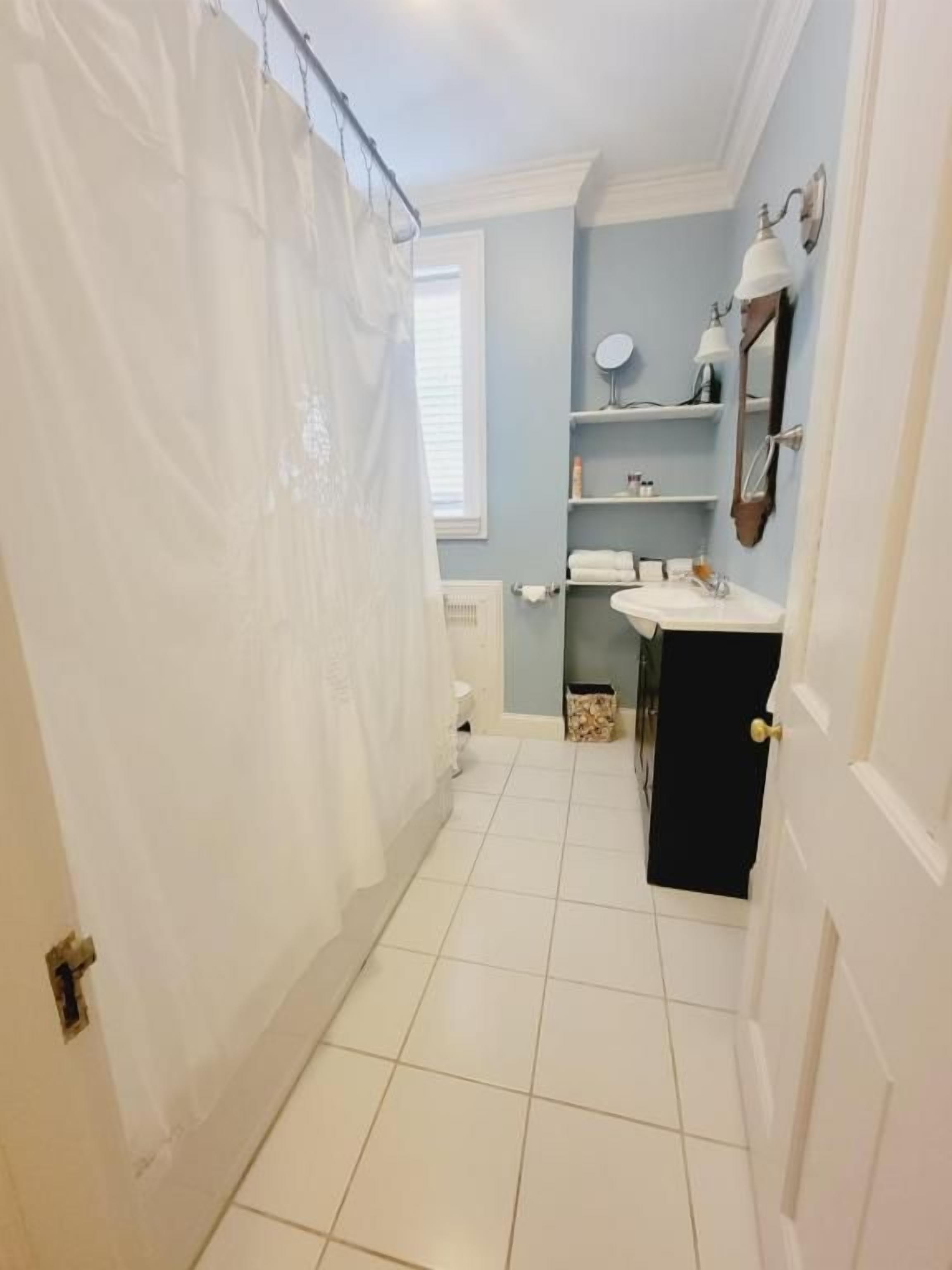A bathroom with a white shower curtain, a sink, a mirror, and a window.