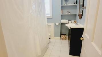 A bathroom with a white shower curtain, a sink, a mirror, and a window.