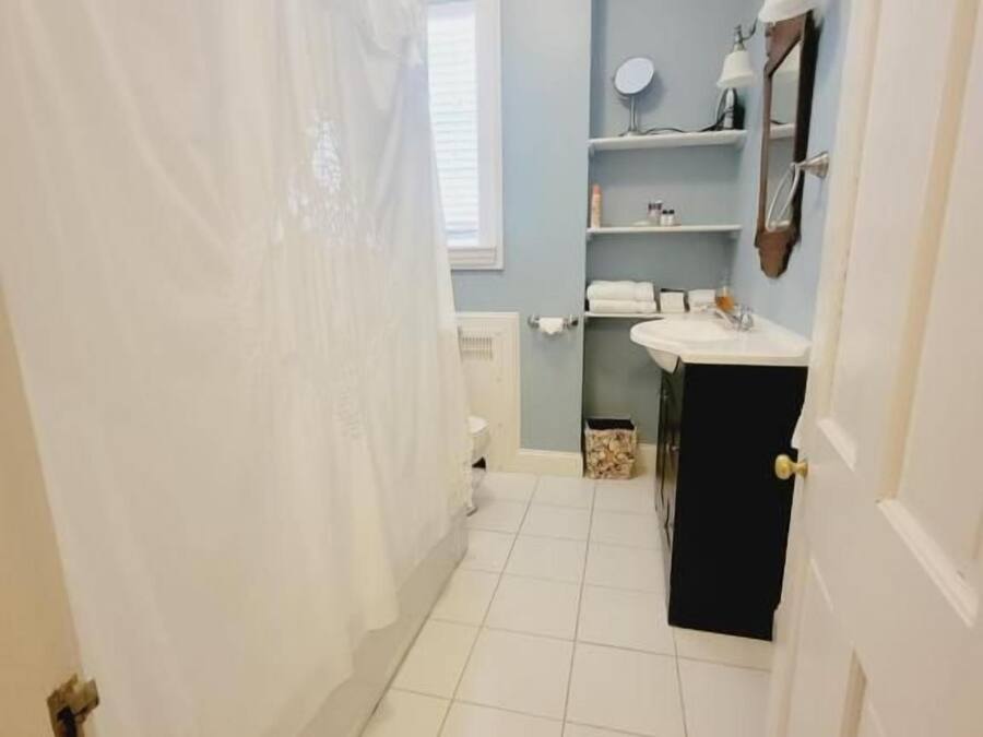 A bathroom with a white shower curtain, a sink, a mirror, and a window.