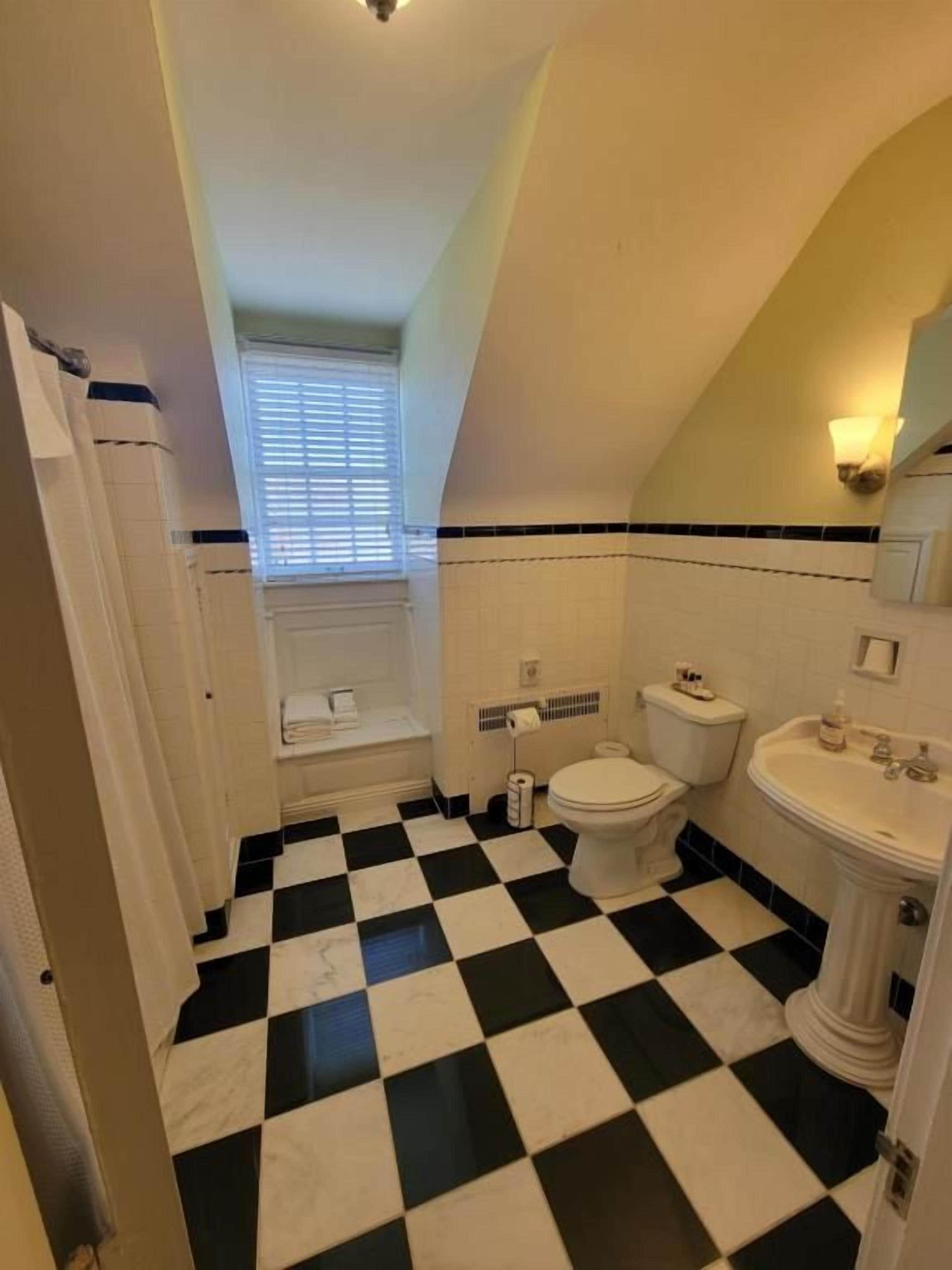 A bathroom with a checkered floor, a toilet, a sink, and a window with blinds.