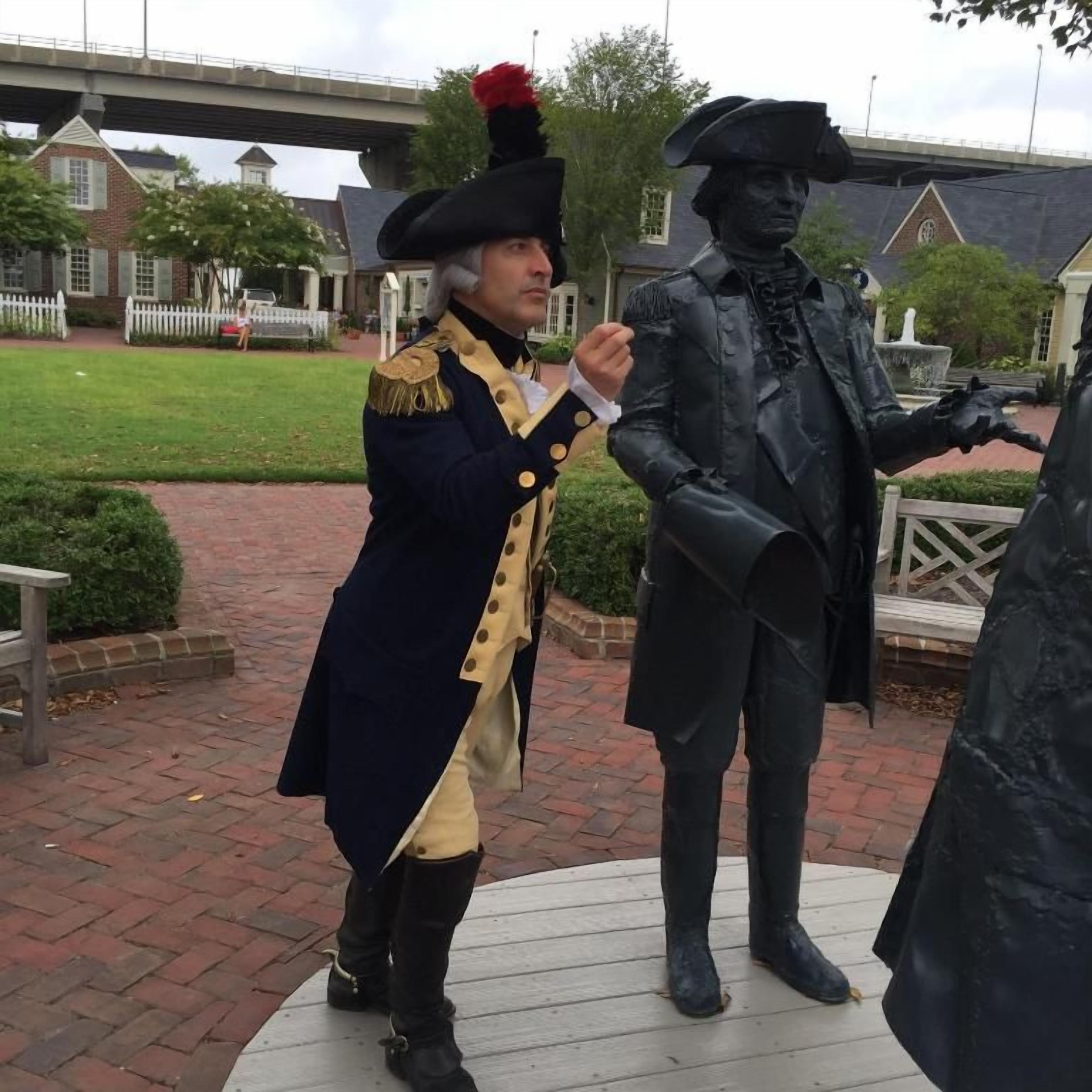 Une personne vêtue d’un costume d’époque, debout à côté d’une statue.