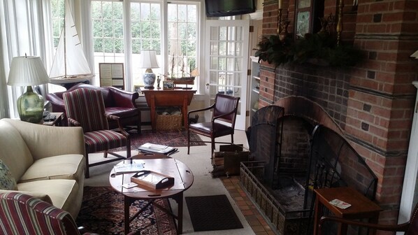 A cozy living room with a fireplace, a sofa, a striped armchair, and a coffee table. - Hornsby House Inn (Yorktown)