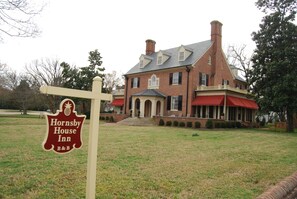 A large brick building with a red awning, a sign for Hornsby House Inn, and a well-maintained lawn. - Hornsby House Inn (Yorktown)