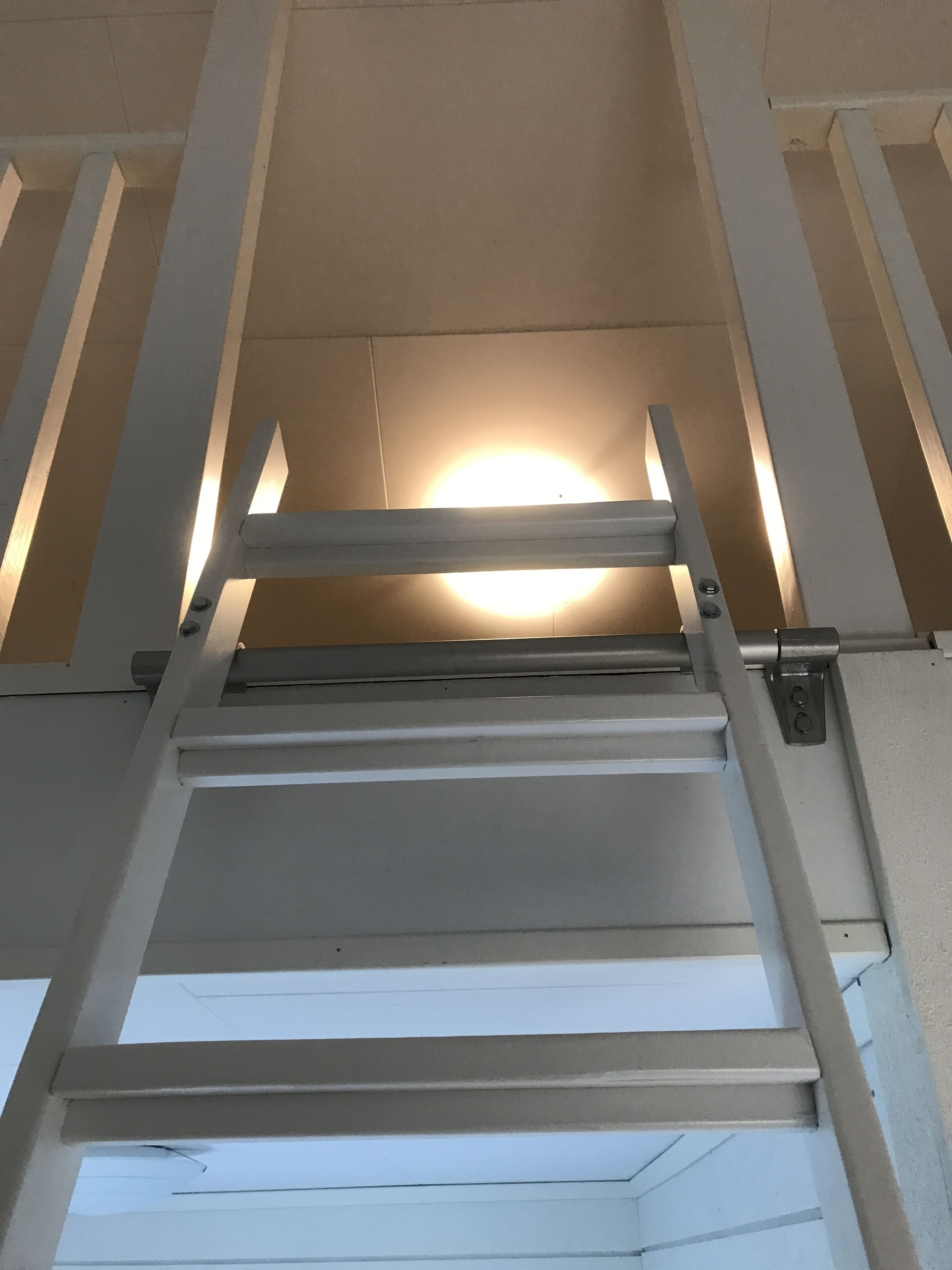 Una escalera metálica que conduce a un techo con una lámpara circular.