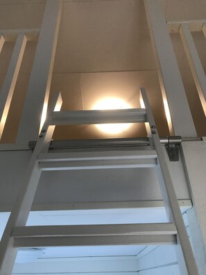 Une échelle métallique menant à un plafond sur lequel est fixé un luminaire circulaire.
