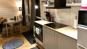 A compact kitchen with a dining area, a built-in oven, a coffee maker, and a variety of kitchen utensils on the countertop. - Hills Loft Cottage with Sauna (Gränna)