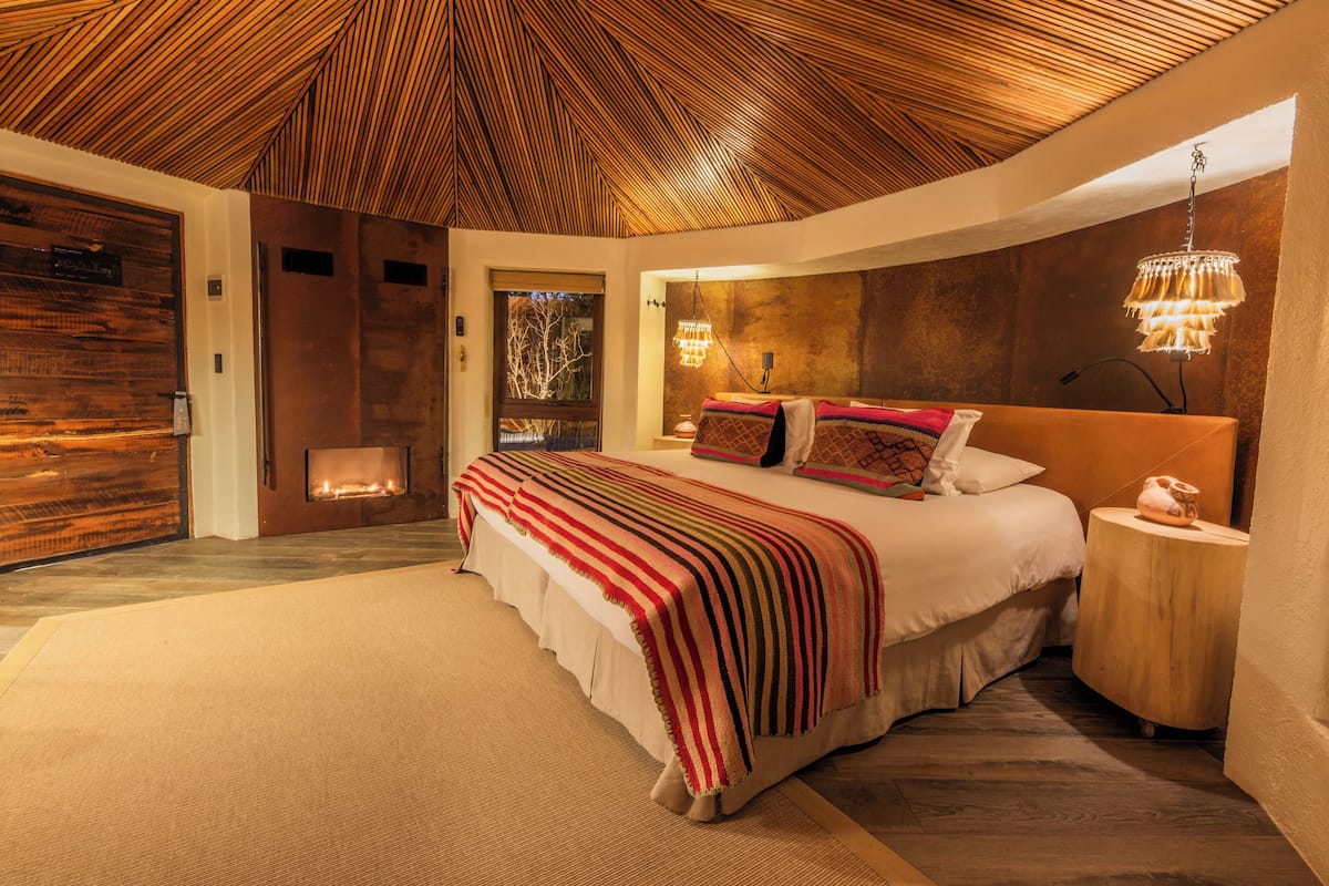 Un dormitorio moderno con una cama grande, techo de madera y chimenea.