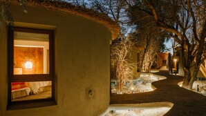 Un intérieur chaleureux et bien éclairé, dans un bâtiment de style rustique, avec une chambre visible et un sentier sinueux menant à une autre construction.