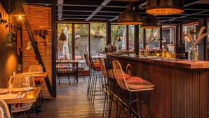 Un restaurant avec des tables en bois, des chaises en osier et des lampes suspendues.