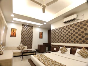 A hotel room with a bed, a sofa, a desk, and a ceiling fan. - Hotel Shiv Villas (Goharganj)