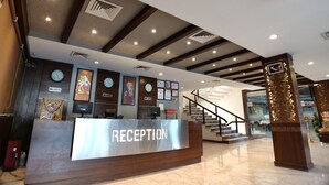 A reception area with a modern design, featuring a reception desk labeled "RECEPTION," multiple clocks displaying different time zones, and a staircase leading to upper floors. - Hotel Shiv Villas (Goharganj)