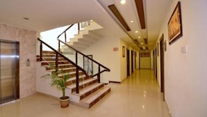 A hotel lobby with a marble floor, a staircase with a glass railing, and an elevator. - Hotel Shiv Villas (Goharganj)