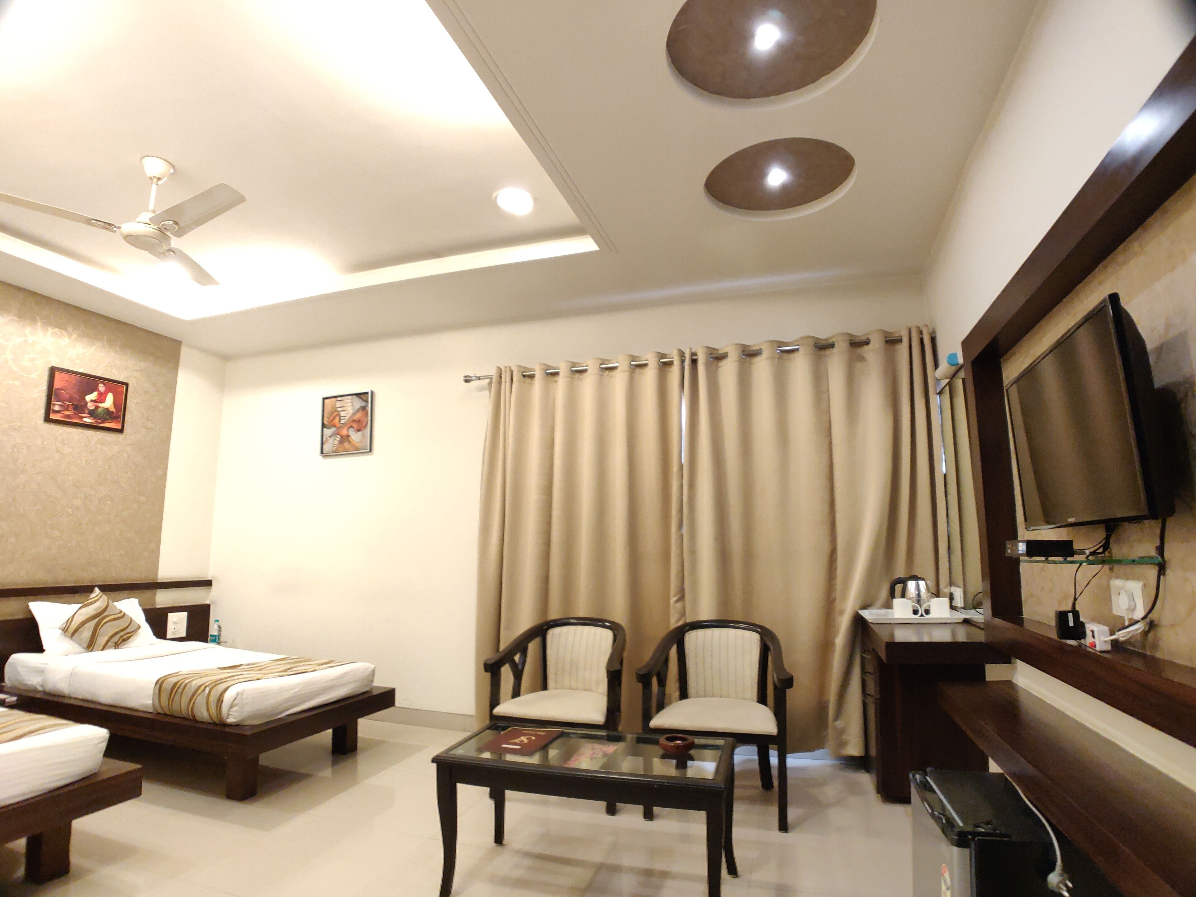 Une chambre d’hôtel comprenant un lit, deux fauteuils, une table basse, un ventilateur de plafond, une télévision et un rideau.