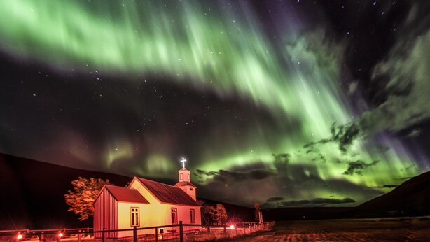 A church with a cross on the steeple, surrounded by a fence and a field. - Bólstaðarhlíð Cottage (Blönduós)
