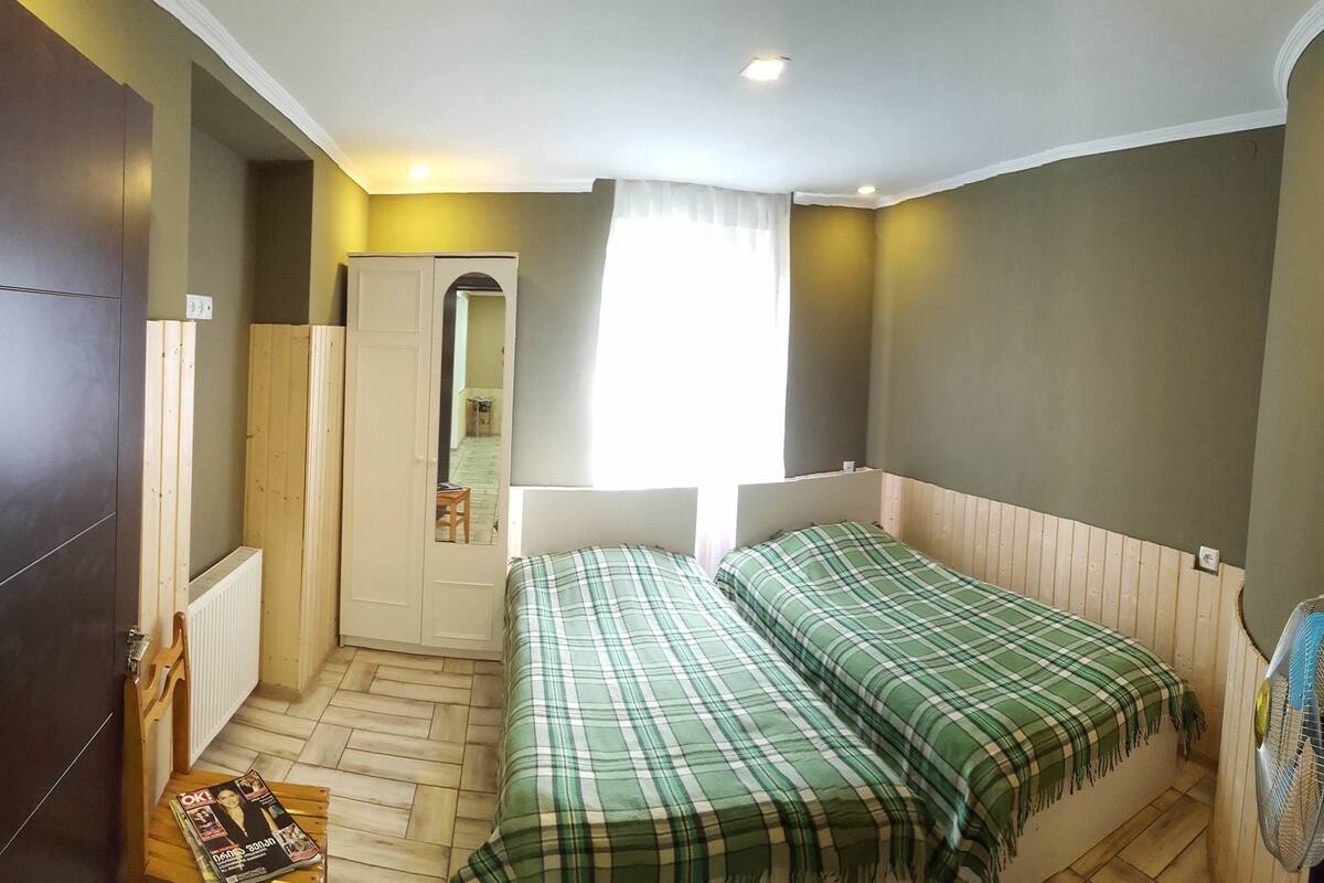 A bedroom with two beds, a wardrobe, a radiator, and a window with curtains.