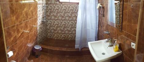 Un baño con ducha, inodoro y lavamanos, con un papel tapiz decorativo y una ventana.