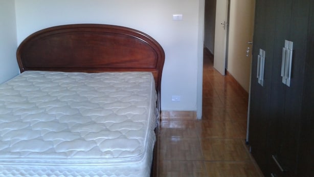 Un dormitorio con cabecera de madera, colchón, armario y suelo de baldosas.