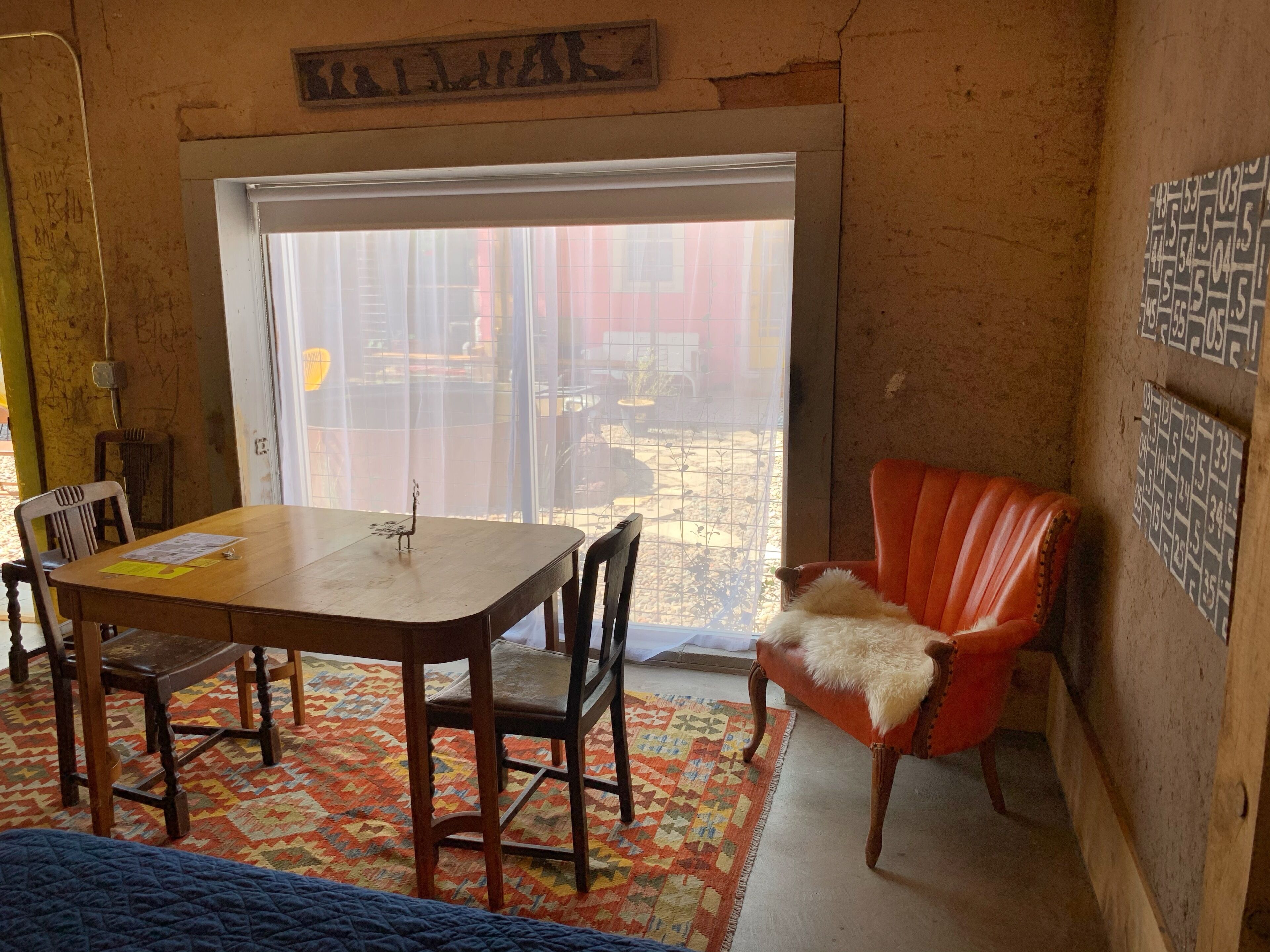 A room with a wooden table, chairs, a red leather chair, a patterned rug, and a view through a window.