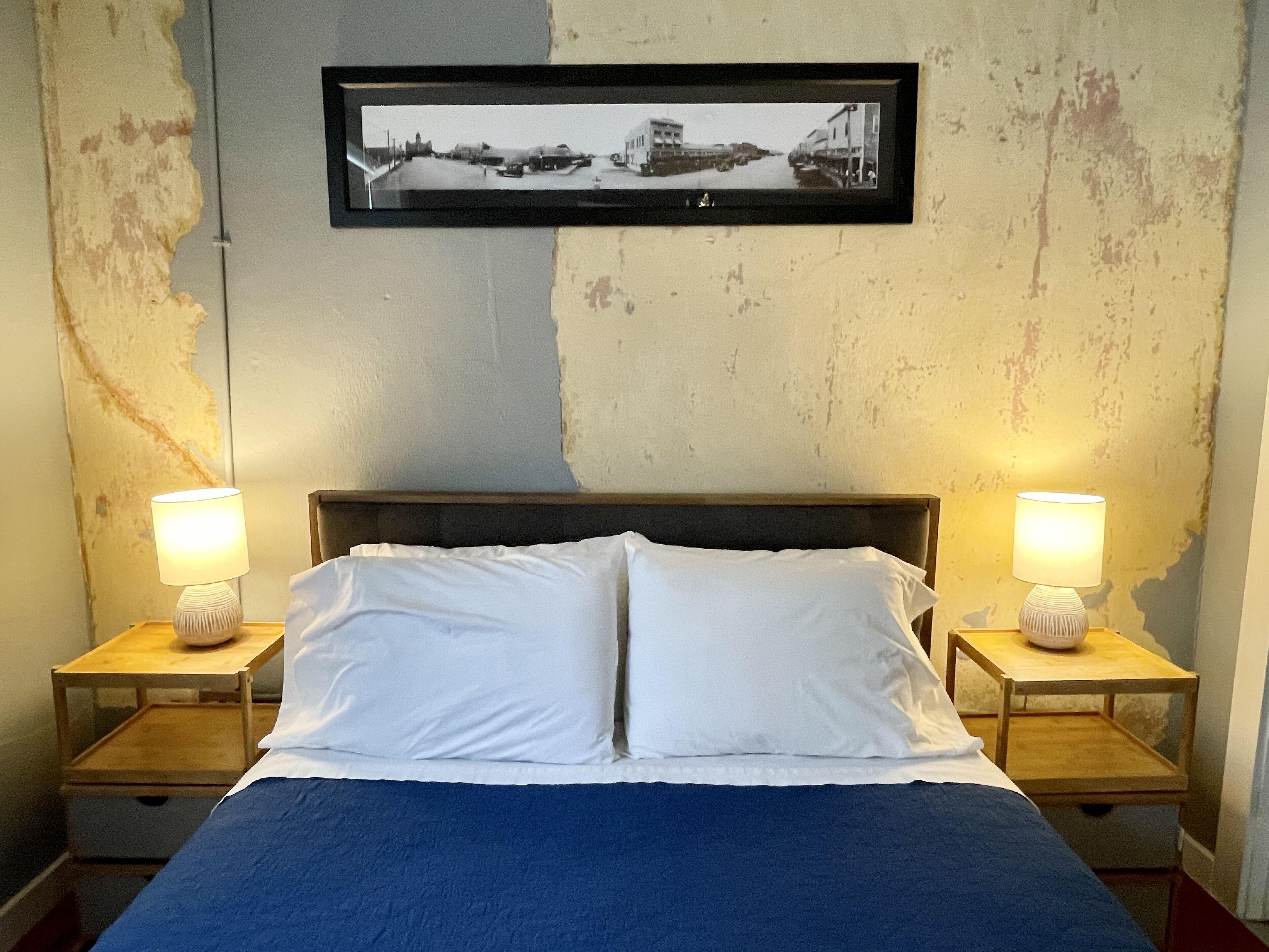 A bedroom with a bed, two bedside tables with lamps, a framed picture on the wall, and a textured wall.