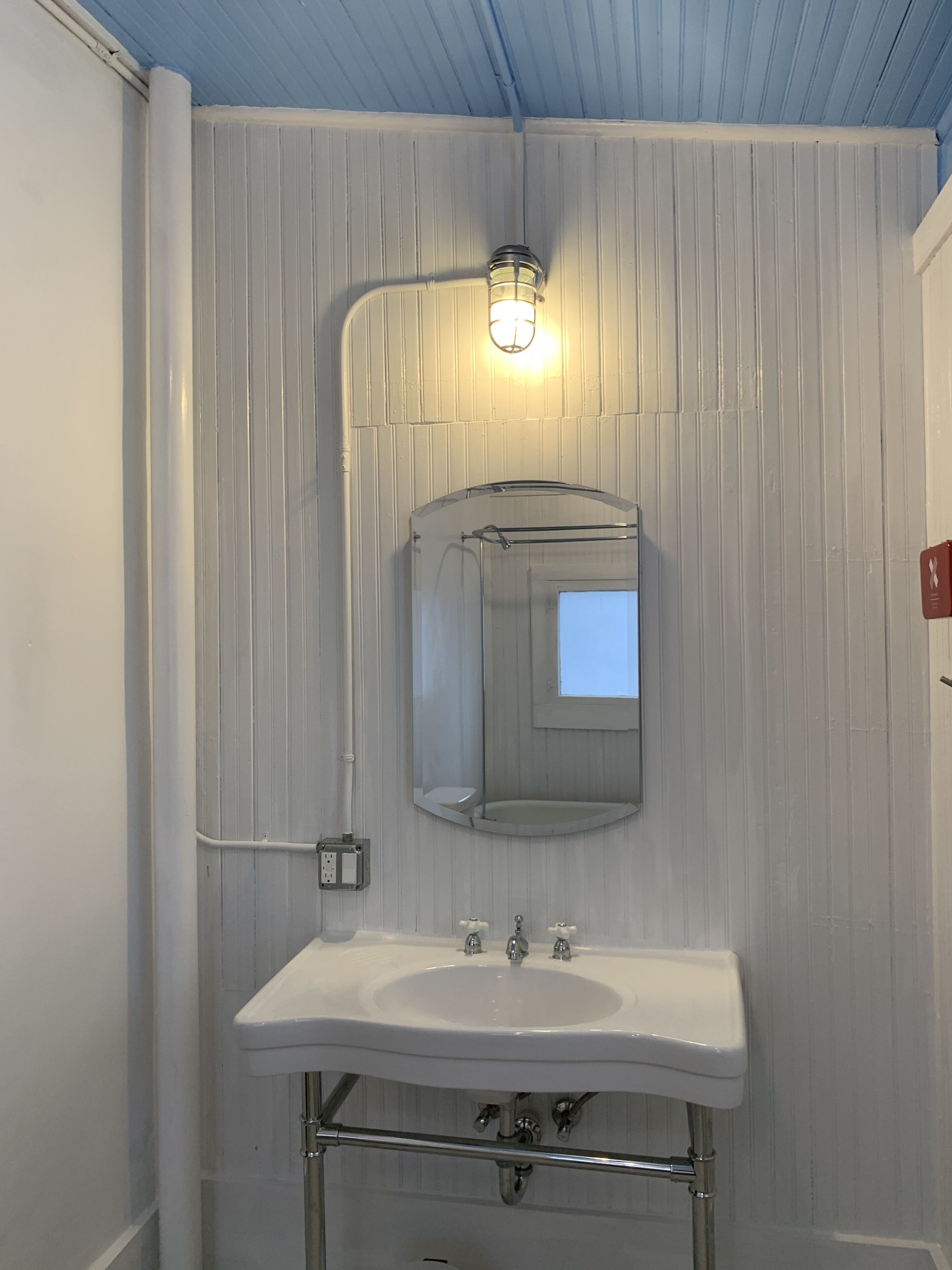 A bathroom with a white sink, a mirror, and a light fixture above the mirror.
