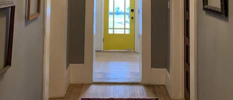 Un couloir orné d’un lustre, de tableaux encadrés et d’une porte jaune.