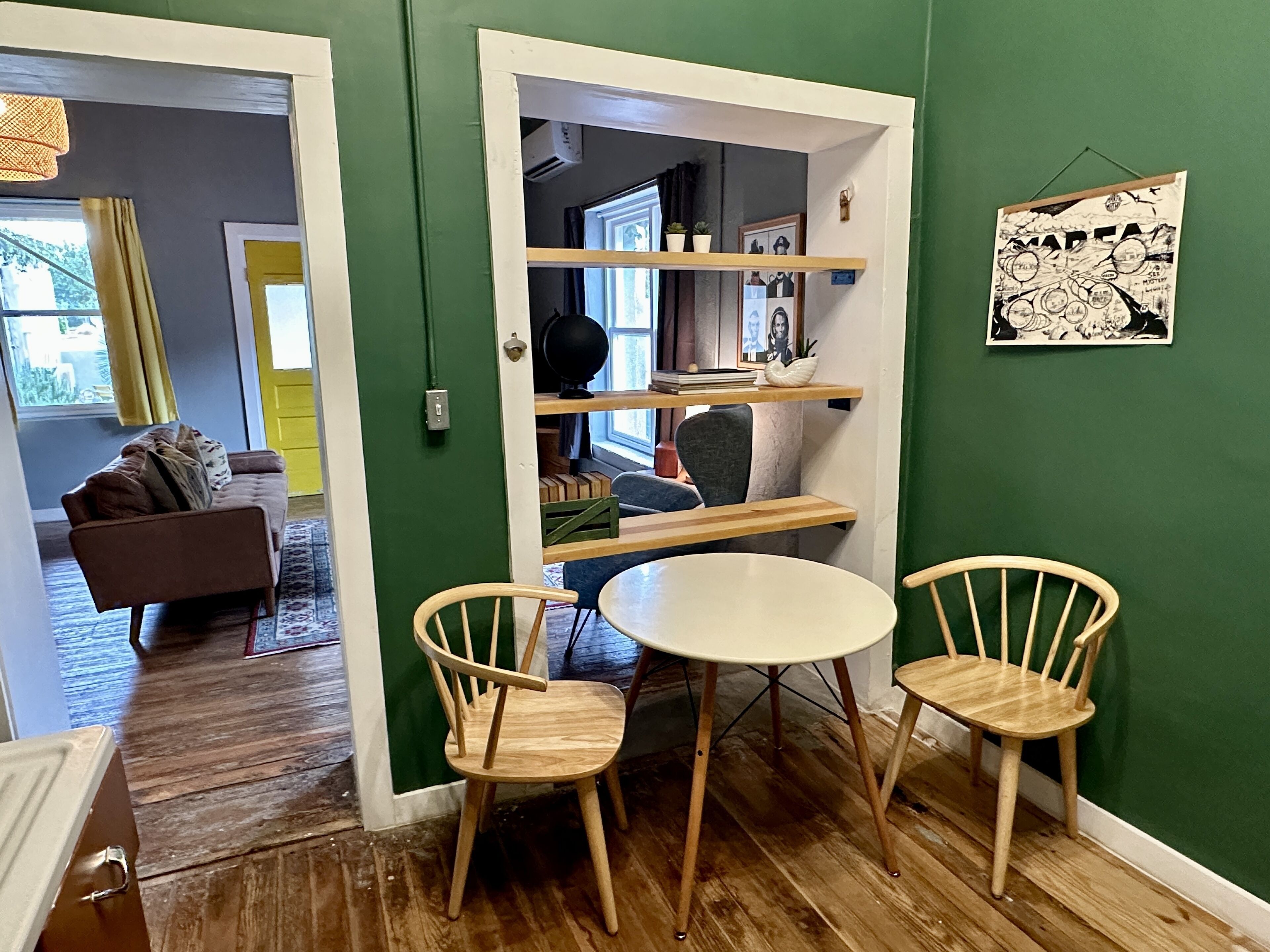 A room with a wooden dining table and chairs, a sofa, and a bookshelf.